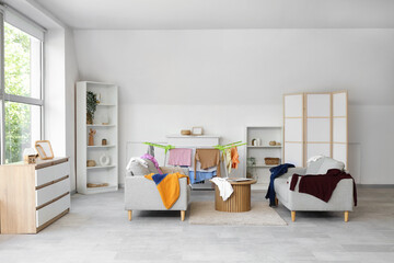 Interior of living room with dryer and dirty laundry on sofas