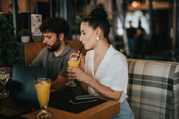 Colleagues having a business meeting at a coffee bar, enjoying orange juice, and discussing work while using a laptop.