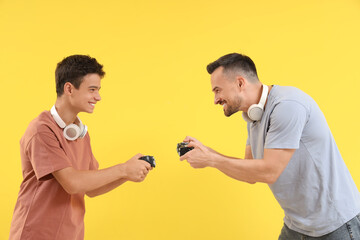 Teenage boy with his father playing video game on yellow background