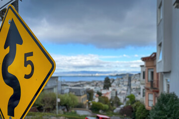 Traffic sign allowing speed of 5 mph due to winding road at Lombard Street against blue sky with blurred cityscape of San Francisco, California, USA