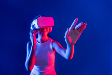 Smart female standing with surrounded by cyberpunk neon light wear VR headset connecting metaverse, futuristic cyberspace community technology. Woman using hand touching virtual object. Hallucination.