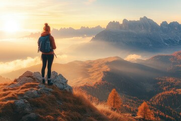 Fototapeta premium Young woman on mountain peak and beautiful mountain valley in haze at colorful sunset in autumn. Dolomites, Italy. Sporty girl, mountain ridges in fog, orange grass, golden sun in fall. Hiking, ai