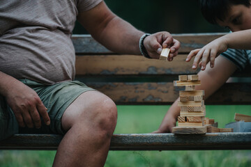 A father and son enjoy quality time playing building blocks on a park bench, focusing on bonding and creativity.