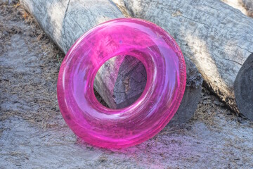 one plastic pink round inflatable swimming ring lies on a gray tree log and the ground on a summer street