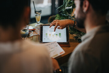 Businesspeople discussing data and charts on a tablet during a meeting at a coffee bar....