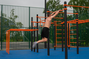A shirtless man is doing a workout on the horizontal bars outdoors.