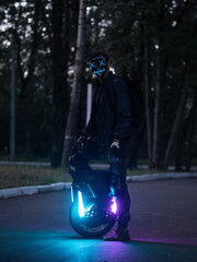 A young man in a luminous mask on a electric monowheel in the park. Halloween concept © pavelkant