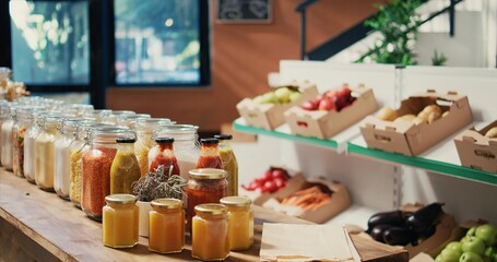Bulk merchandise in reusable glass jars sold at zero waste store to protect environmental changes, natural homemade sauces. Eco friendly market with organic grains, spices and cereals. Handheld shot.