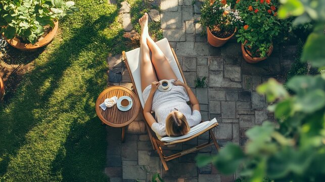 A woman relaxes in a garden lounge chair enjoying tea during a sunny afternoon surrounded by blooming flowers and greenery - Powered by Adobe