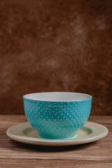 Empty blue and textured blue turquoise ceramic bowl over plate. Wooden table and brown blurred background.