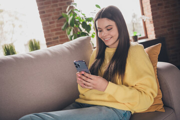 Portrait of nice teen girl sit couch hold device relax wear yellow clothes modern interior flat indoors