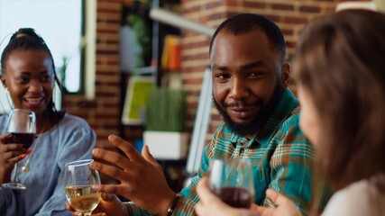 African american man entertaining friends at house party, making them pay attention to interesting story. Guest making BIPOC women laugh in living room while enjoying drinks and charcuterie platter