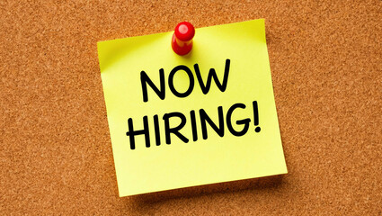 now hiring word written on a note sticky on corkboard