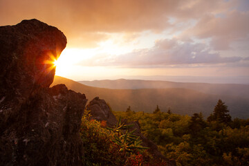 Sun shining around big rock boulder at the edge of mountain range at sunset