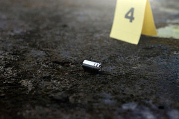 Pistol bullet shell and blurred number 4 on yellow paper on cement floor which has dirt and...