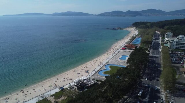 Aerial view of Playa de Samil, the main beach of Vigo in Galicia in northwest Spain. Sunny day, crystal clear blue sea. Houses, streets. Drone take.