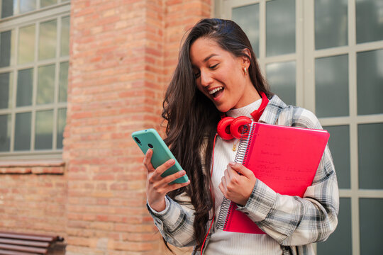 One latina student using her smartphone to share on the social media app. Hispanic teenager having fun with a cellphone, Latin female browsing on internet with a mobile phone at university campus