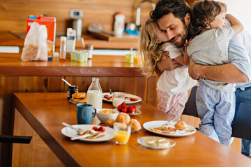 Father hugging children during breakfast at home