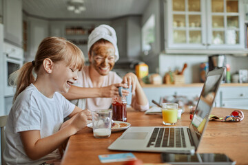 Happy mother and daughter having breakfast with monitor in kitchen