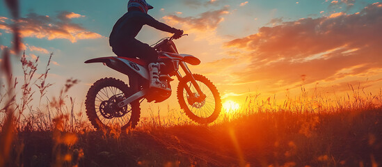 A man is riding a dirt bike in a field with a beautiful sunset in the background