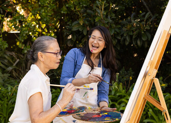 Obraz premium Painting on canvas, Asian granddaughter and grandmother enjoying outdoor art activity together