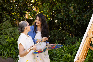 Obraz premium Painting together outdoors, asian granddaughter and grandmother enjoying activity with brushes