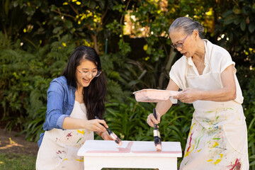 Fototapeta premium Painting table, asian granddaughter and grandmother enjoying outdoor diy project together in garden