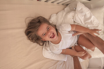 the little girl playing and tickling on the bed and having fun