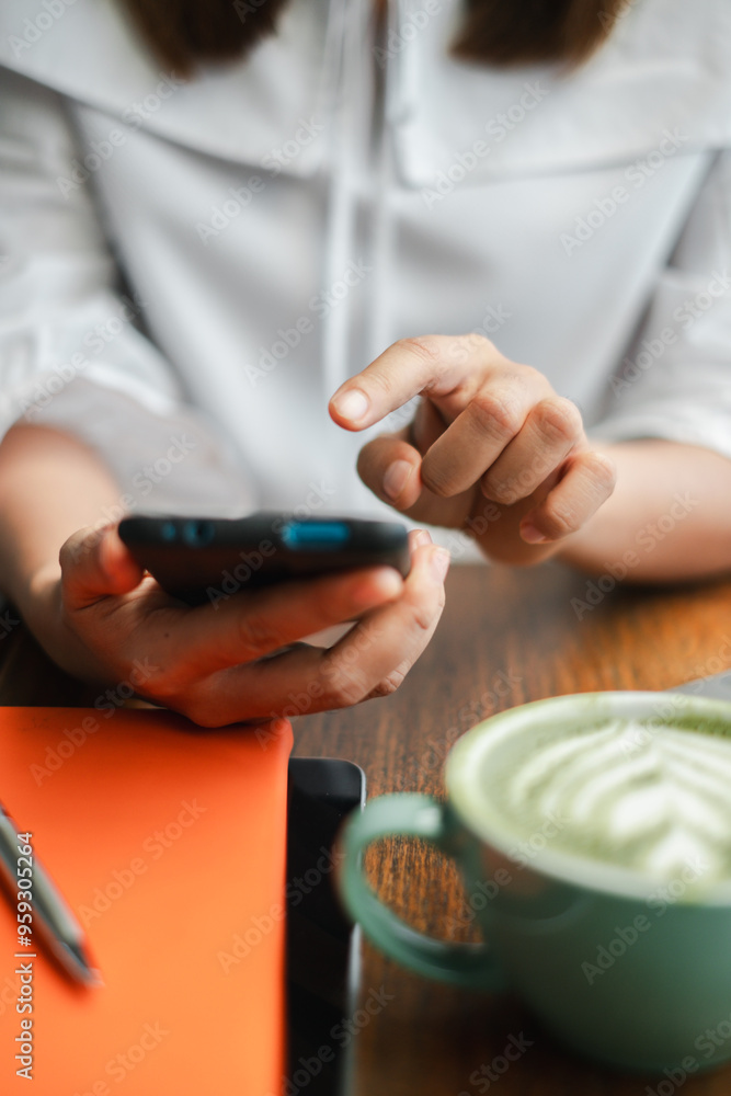 Poster a close-up shot of a person using a smartphone at a coffee shop, with a latte and a notebook on a wo