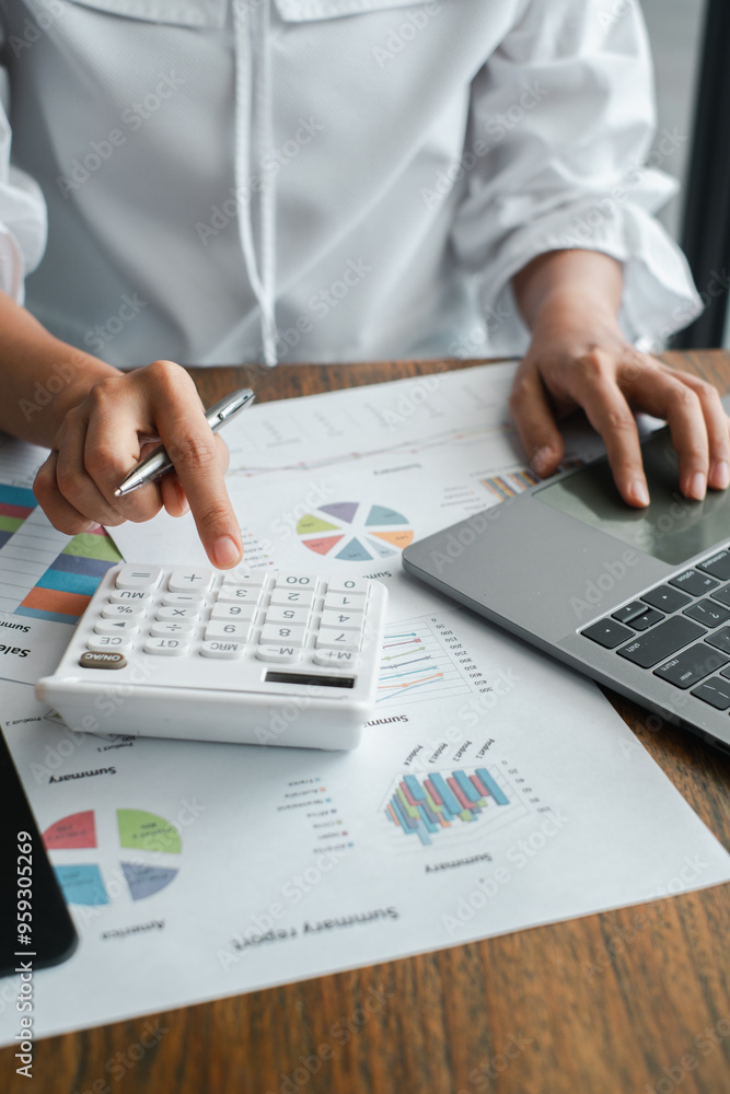 Poster close-up of a business professional using a calculator and laptop for financial analysis with graphs