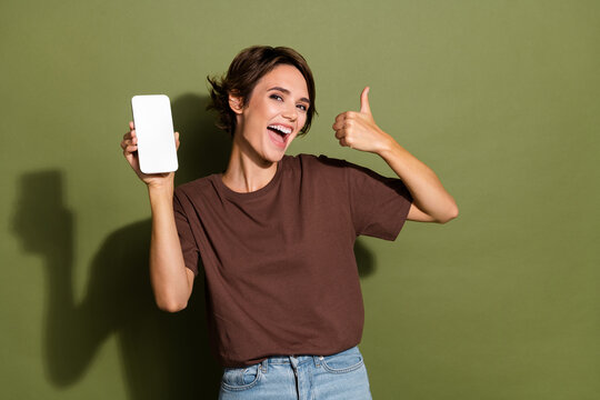 Photo portrait of pretty young girl hold telephone show cheerful thumb up dressed stylish brown outfit isolated on khaki color background