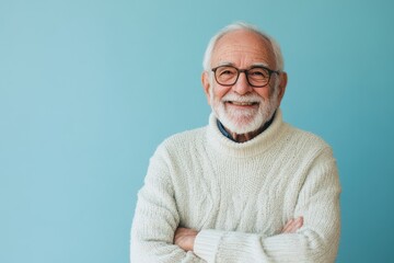Obraz premium Elderly male presenter, smiling, in a casual sweater, in front of a solid light blue background with space for messaging