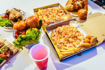 An indoor office party scene with no people around, featuring a desk filled with food pizza, bread, salad, chicken grill, French fries, and beer set against a night light with RGB lighting.