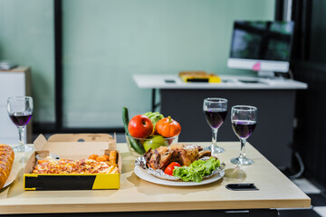 A business office is set for a Halloween party, with food spread across a desk pizza, bread, chicken grill, French fries, salad, and beer ready for celebration, but no people present.