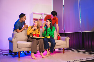 A group of Asian friends gathers in an office for a night of BBQ, pizza, and drinks, celebrating Halloween with vibrant RGB lighting, laughter, and cheering for their favorite soccer team.