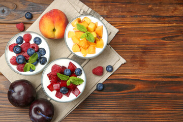 Tasty yogurt with fresh berries, fruits and mint in glasses on wooden table, flat lay. Space for text