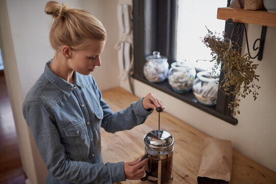 Woman, coffee and french press in kitchen for beverage in morning for relax on weekend or holiday. Female person, caffeine and plunger on counter for cappuccino drink, latte or preparation at home - Powered by Adobe