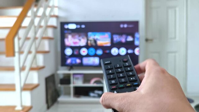Turn on and turn off the TV remote, watching tv close up hand with remote control switches channels tv on background out of focus