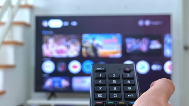 Turn on and turn off the TV remote, watching tv close up hand with remote control switches channels tv on background out of focus