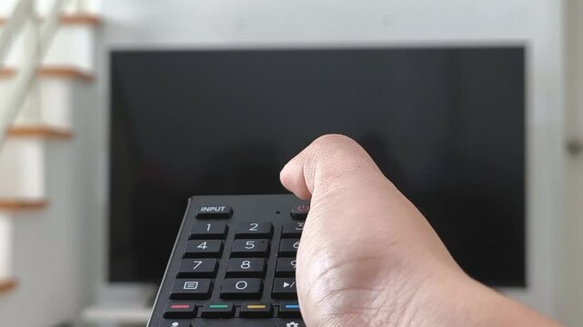 Turn on and turn off the TV remote, watching tv close up hand with remote control switches channels tv on background out of focus