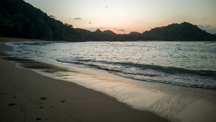 Tropical beach with rocks reflecting sunshine in the wet sand in Malang, Indonesia