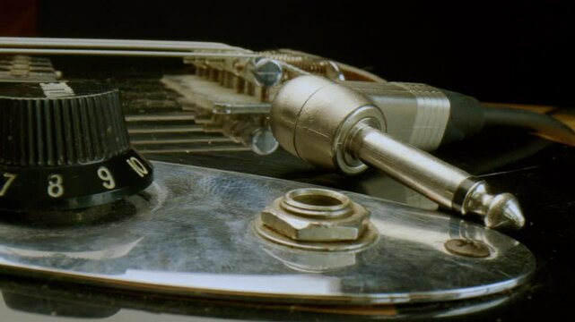 Cable jack resting near socket on electric guitar body with control knobs, metal pickguard and strings. Extreme close-up shot