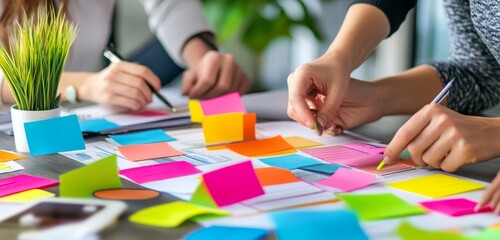 Closeup of hands working on a sticky note brainstorming session on a table.