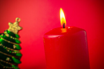 Red Candle and Christmas Tree Ornament against Red Background - Festive Holiday Decoration