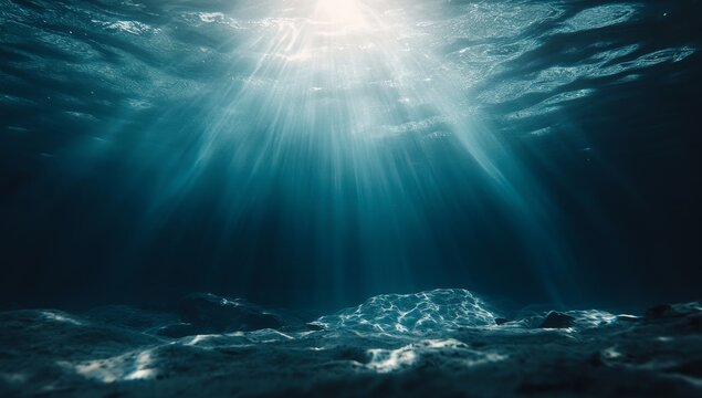 Sunlight beams through the deep blue ocean water, illuminating the sandy seafloor.
