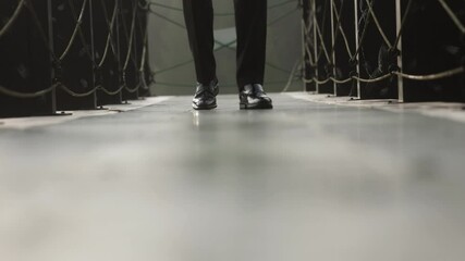Close up of legs of man in black suit walks confidently across tiled pier over misty lake with fog in the early morning light. Man walks towards camera with purpose, exuding elegance and confidence.