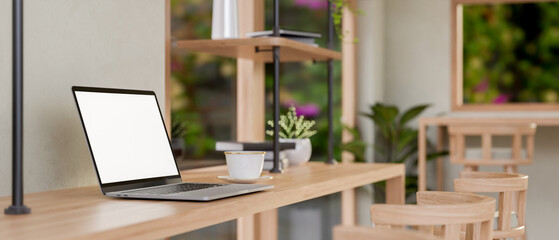 A laptop on a wooden table in a contemporary Scandinavian coffee shop seating area.
