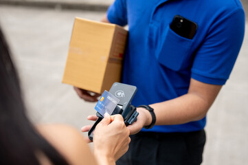 A customer tapping her credit card on a card reader before receiving a package from a delivery man.