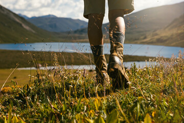Hiker legs wearing leather boots hiking on high altitude mountain top,with a lake in the distance