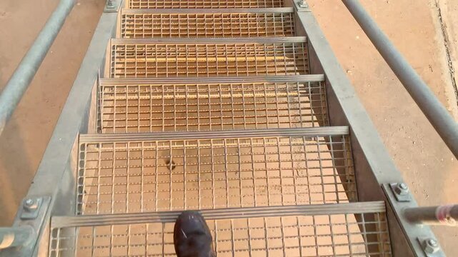 Metal Stairs Leading Upwards. A person walking up a set of metal stairs, the view from the top of the stairs shows a grated platform